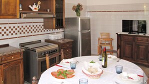 A kitchen with wooden cabinets, a stove, a refrigerator, and a dining table set for two with plates, glasses, and a bottle of wine.