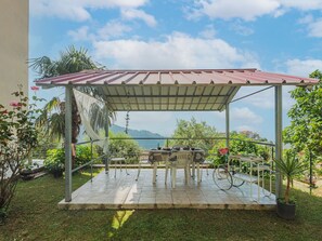 A covered patio with a table and chairs, surrounded by potted plants and a view of the sea.