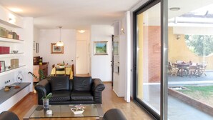 Una sala de estar moderna con una mesa de centro de vidrio, un sofá de cuero negro y un comedor visible a través de una puerta de cristal.