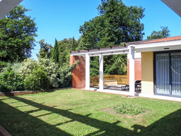 A covered patio area with a brick wall, a wooden fence, and a lawn.