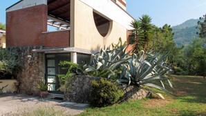 Una casa moderna con base de piedra, un amplio ventanal y un jardín con plantas de agave.