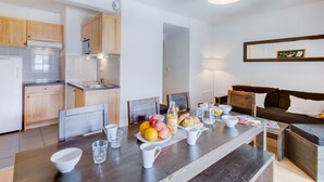 Eine moderne Küche mit Holzschränken, ein Essbereich mit Frühstücksecke und eine Wohnbereich mit Sofa und einem gerahmten Bild an der Wand.