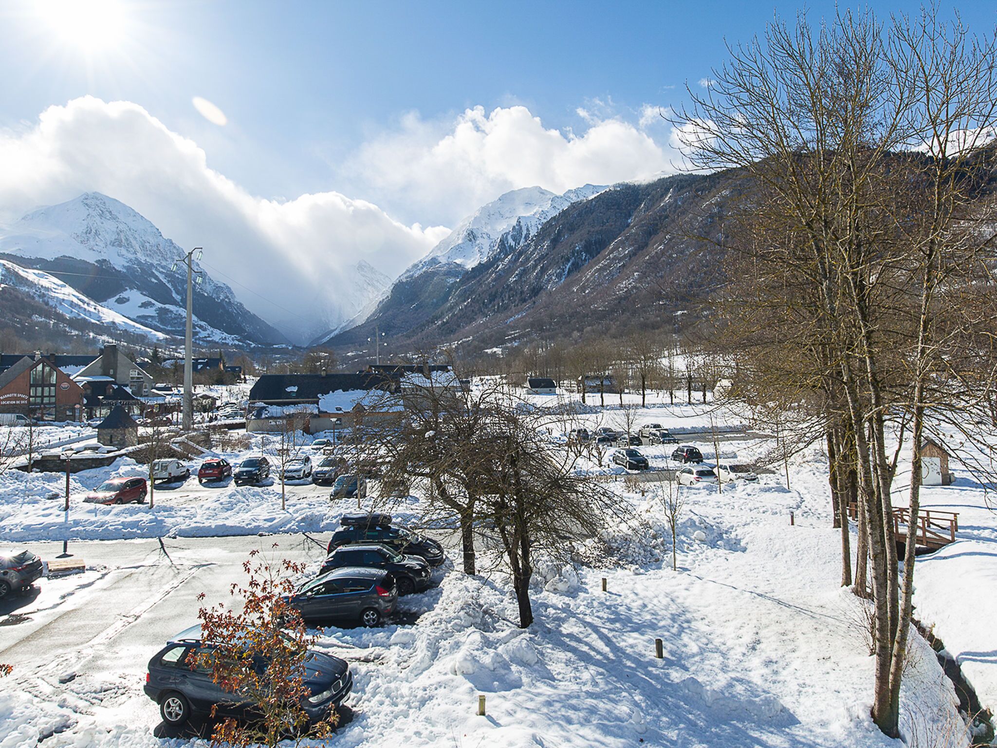 Ein verschneiter Parkplatz mit Autos, ein kleines Gebäude und Berge im Hintergrund.