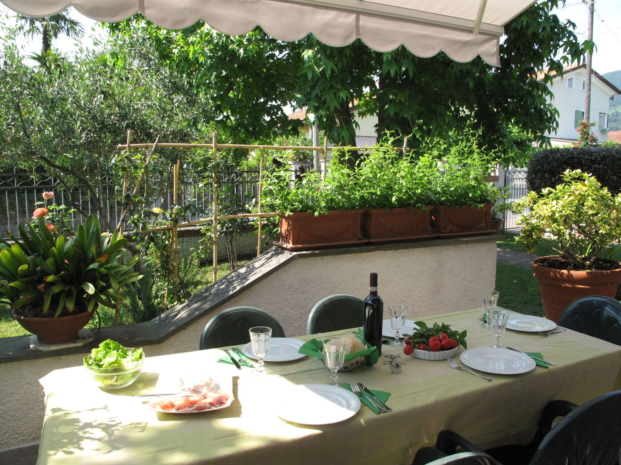 An outdoor dining area with a table set for two, surrounded by potted plants and a garden.