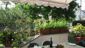 Un área de comedor al aire libre con una mesa dispuesta para dos personas, rodeada de plantas en macetas y un jardín.