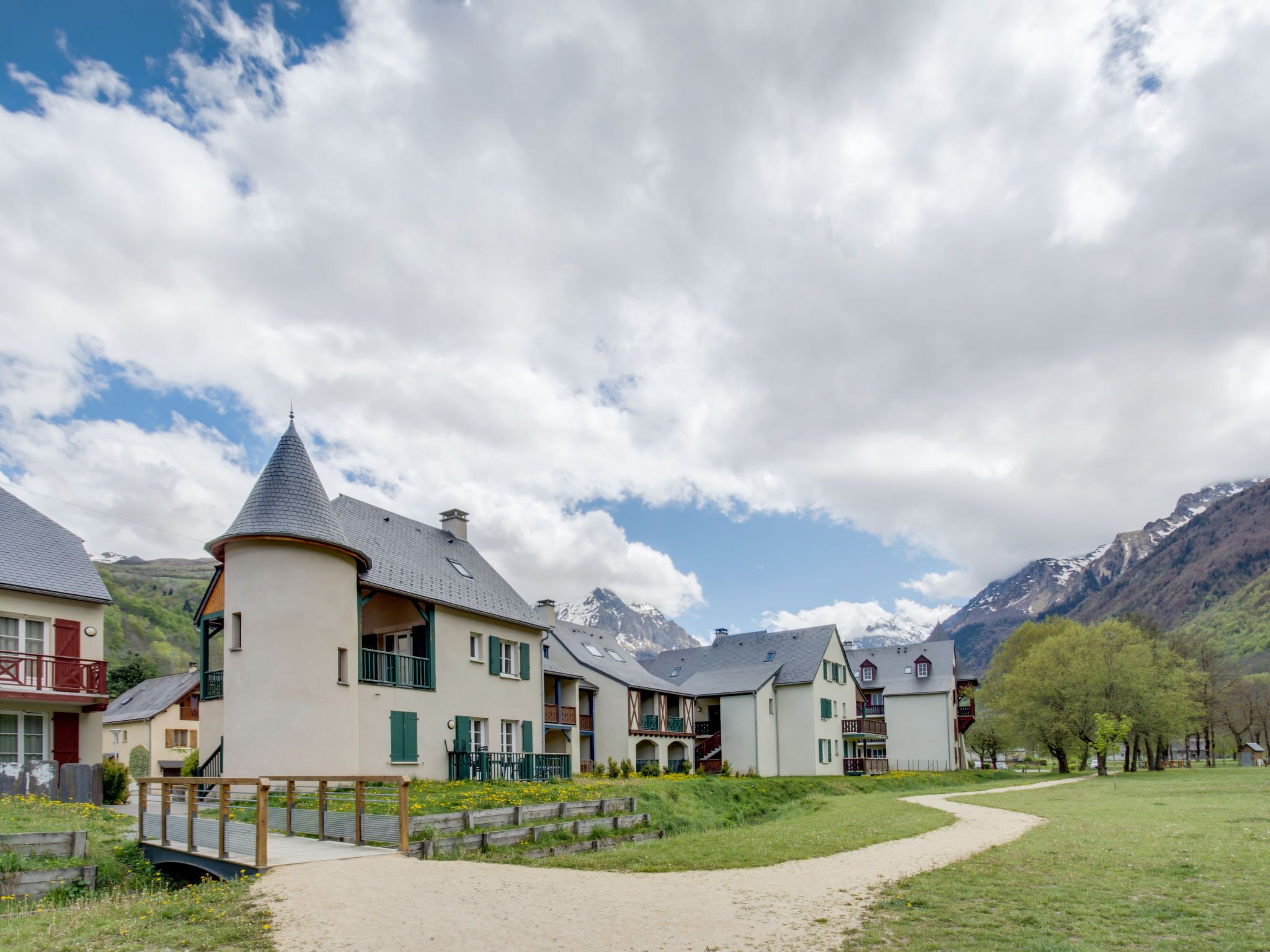 A row of traditional European-style buildings with a central tower, a paved pathway, and a mountainous backdrop.