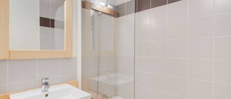 A modern bathroom with a white sink, a mirror, and a glass-enclosed shower area.