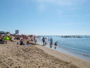 A crowded beach with people sunbathing and swimming.