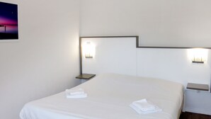 Una habitación de hotel con una cama grande, dos mesitas de noche y luces fijadas en la pared.