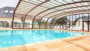 Una piscina interior con techo de vidrio, sillas de descanso y vistas del entorno.