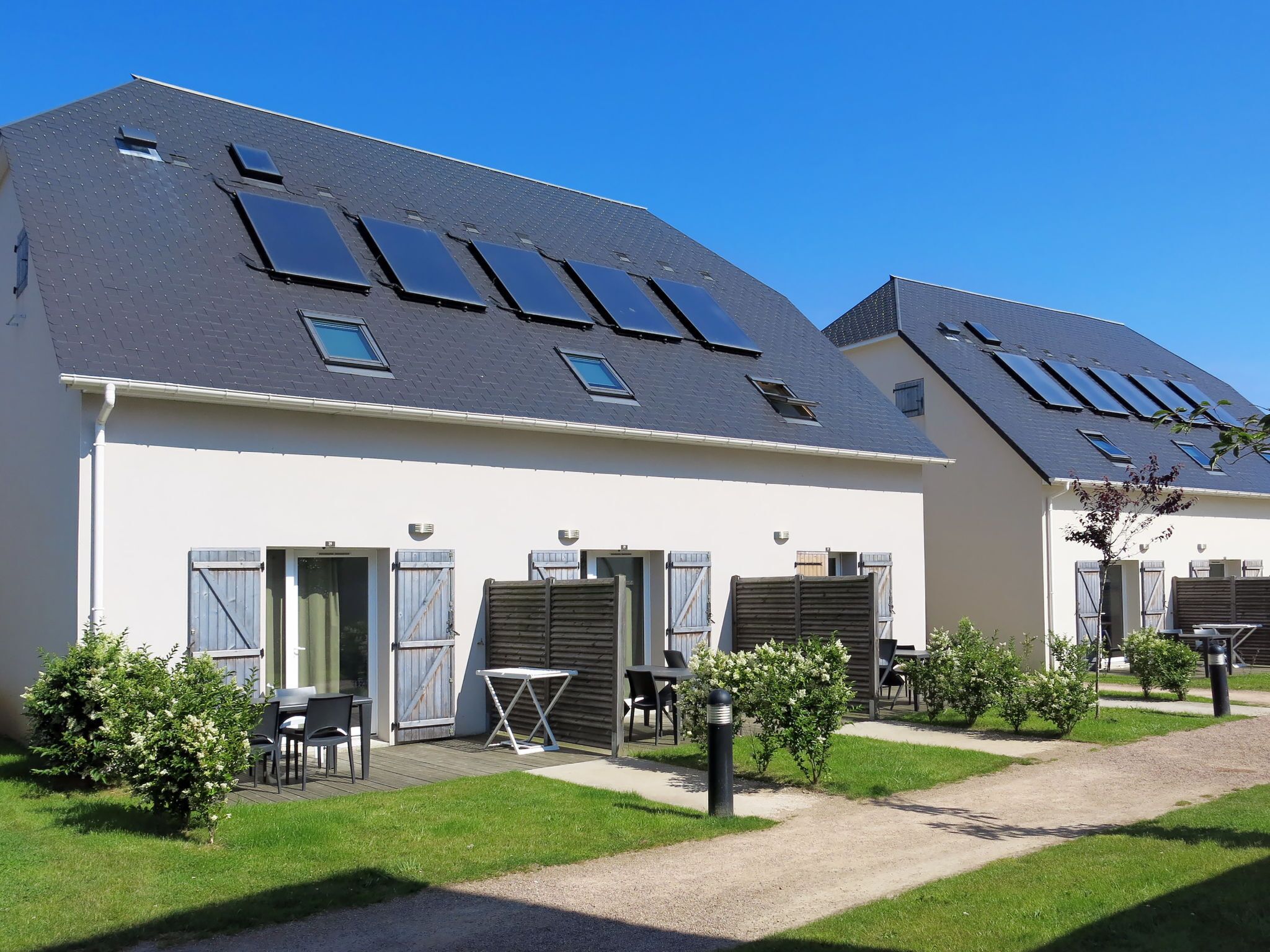 Een rij moderne huizen met zonnepanelen op de daken, een klein terras met buitenmeubilair en een verzorgd gazon.