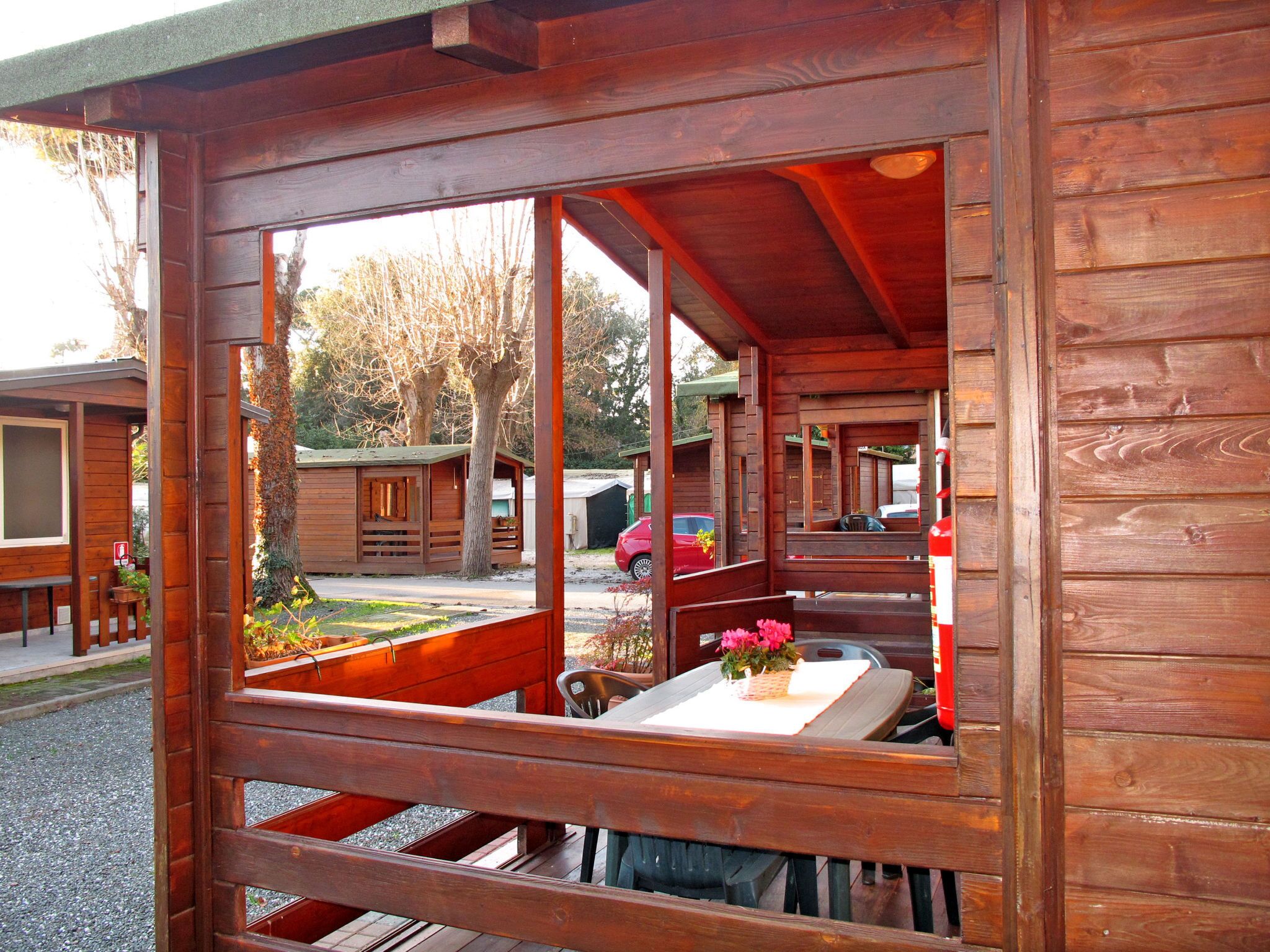 A wooden cabin with a large window, a table with a vase of flowers, and a bench.