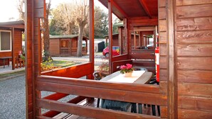 A wooden cabin with a large window, a table with a vase of flowers, and a bench. - Camping Campeggio Italia (MAS370) by Interhome (Marina di Massa)