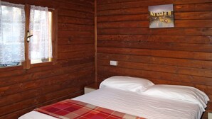 A wooden cabin room with a bed, a window with lace curtains, and a painting on the wall. - Camping Campeggio Italia (MAS370) by Interhome (Marina di Massa)
