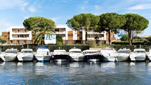 A marina with several boats docked in front of a modern building with balconies and trees.