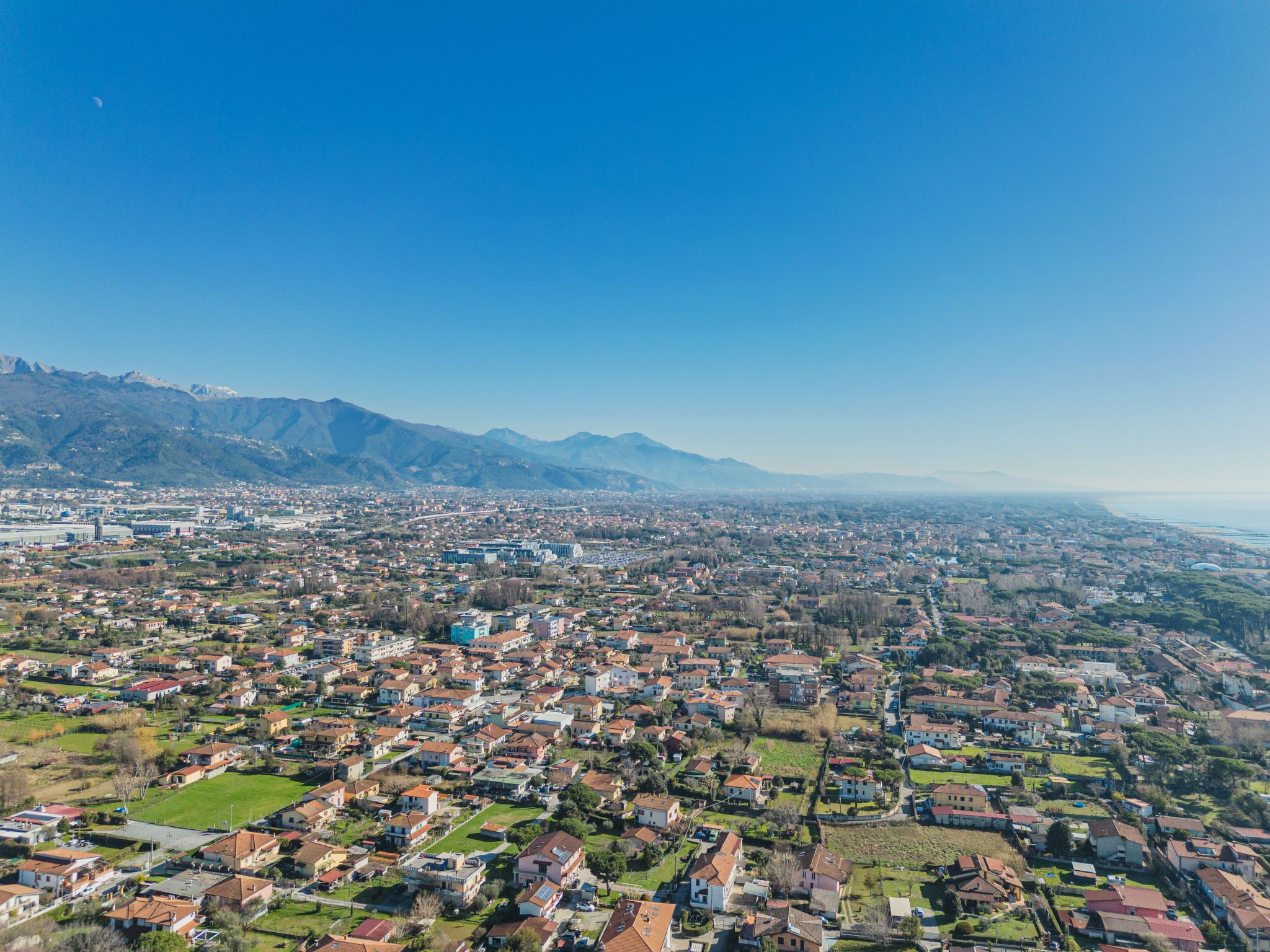 An aerial view of a city with residential areas, a large stadium, and mountains in the background.