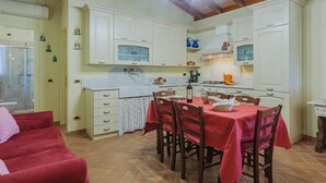 A compact kitchen with white cabinets, a dining table with red tablecloths, and a red sofa in the living area. - Vacation home Colli by Interhome (Marina di Massa)