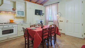 A kitchen with white cabinets, a stove, and a dining table set with red tablecloths and chairs. - Vacation home Colli by Interhome (Marina di Massa)