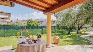 A covered patio with a table set for dining, a green lawn, and a view of houses in the background. - Vacation home Colli by Interhome (Marina di Massa)