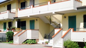 Un edificio residencial de varios pisos con balcones, una escalera central y plantas en macetas.