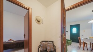 Una habitación con puerta de madera, un banco con almohadones, una mesa de comedor con sillas y un otoman verde.