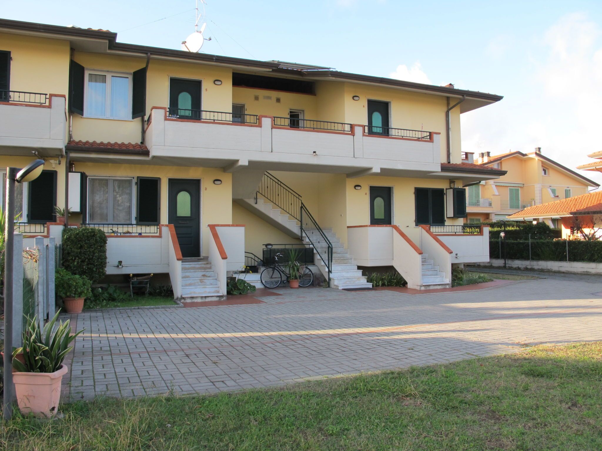 Un edificio residencial de dos pisos con una escalera central, un pequeño balcón y una bicicleta estacionada afuera.