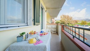 Un balcón con una mesa dispuesta para el desayuno, que incluye frutas, una tetera y tazas.