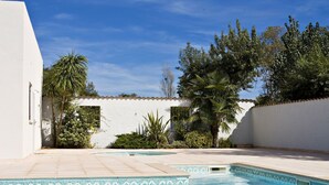 A swimming pool with clear blue water, surrounded by white walls and greenery.