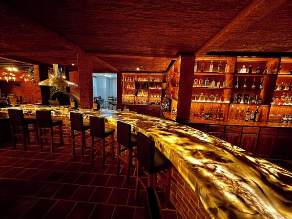 A bar with a long counter, wooden chairs, and shelves of bottles. - Le Suisse Spa (Santa Lucía Milpas Altas)