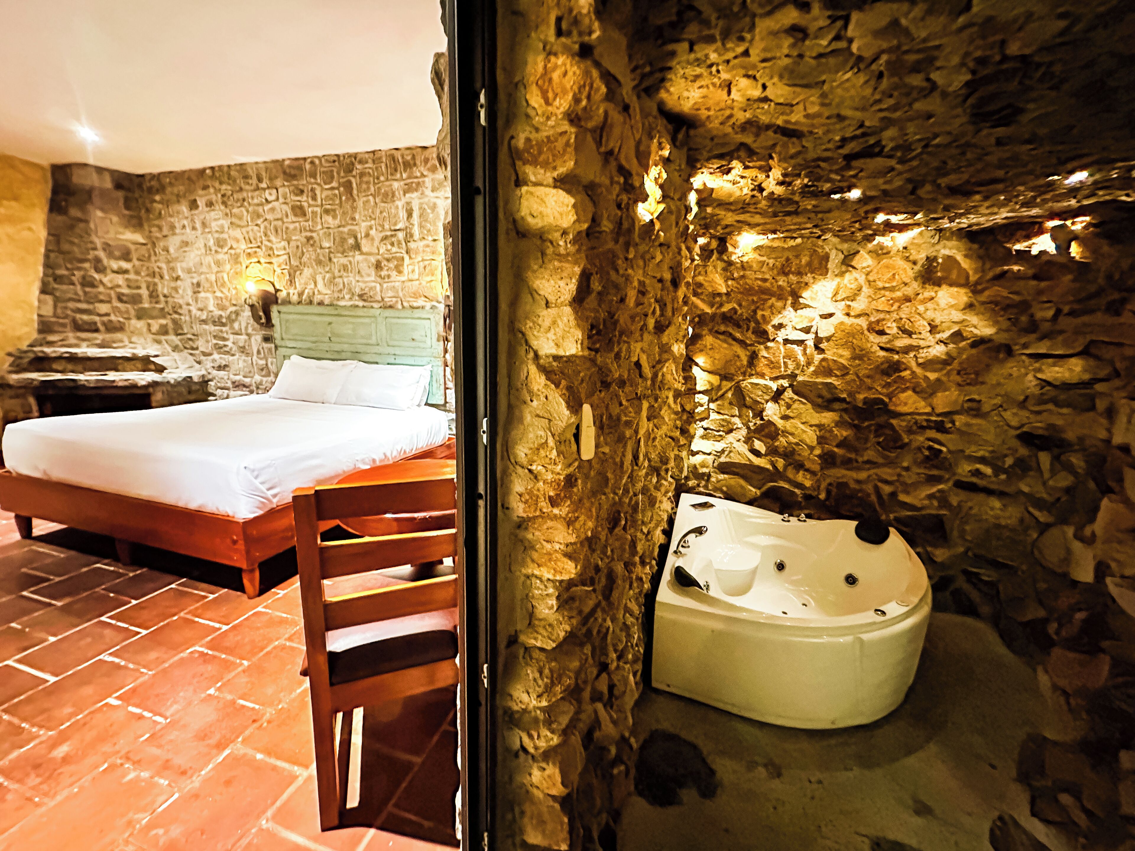 A bedroom with a stone wall, a wooden bed, a nightstand, and a bathtub.