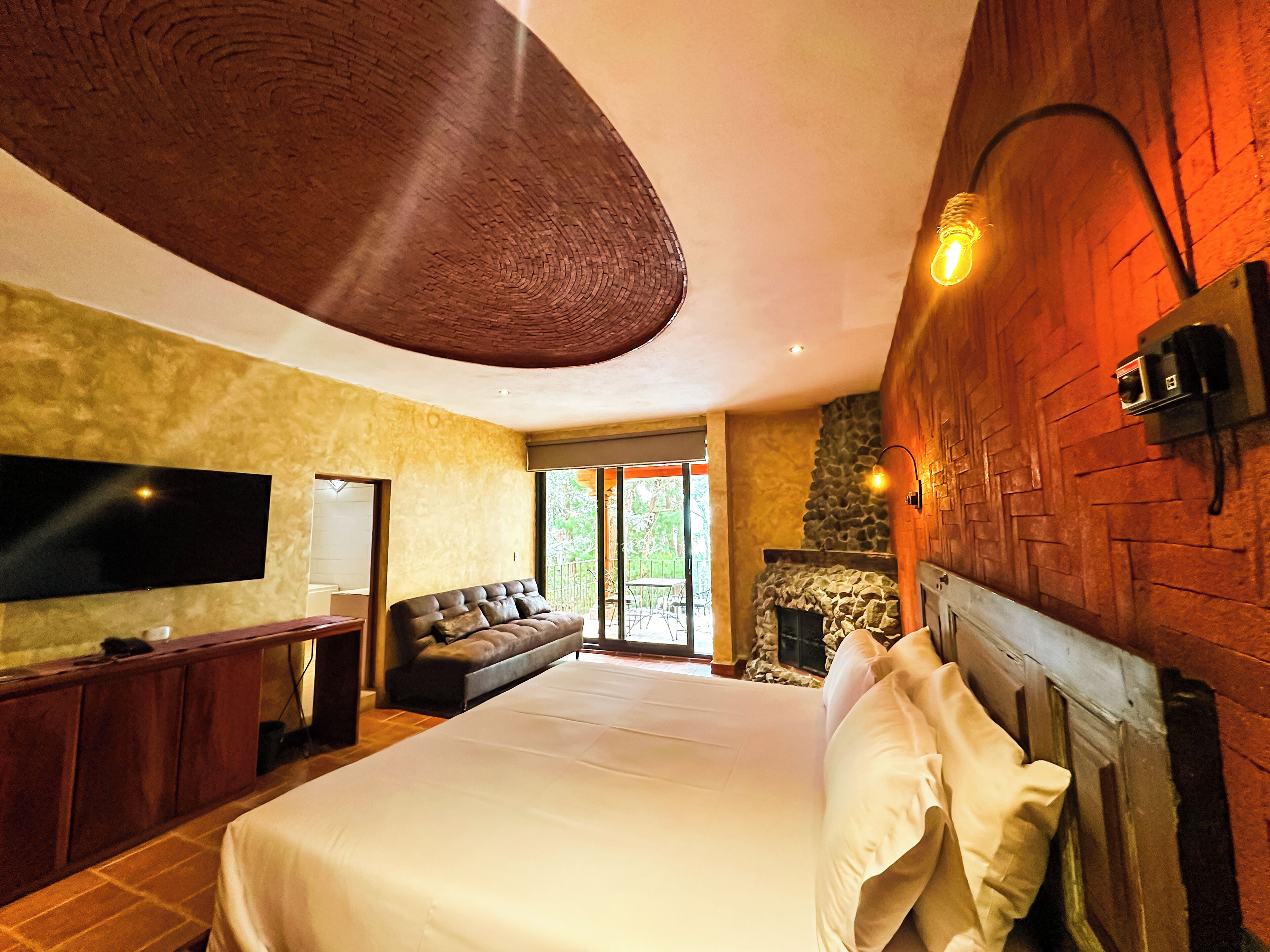 A spacious bedroom with a large bed, a sofa, a flat-screen TV, and a stone fireplace.