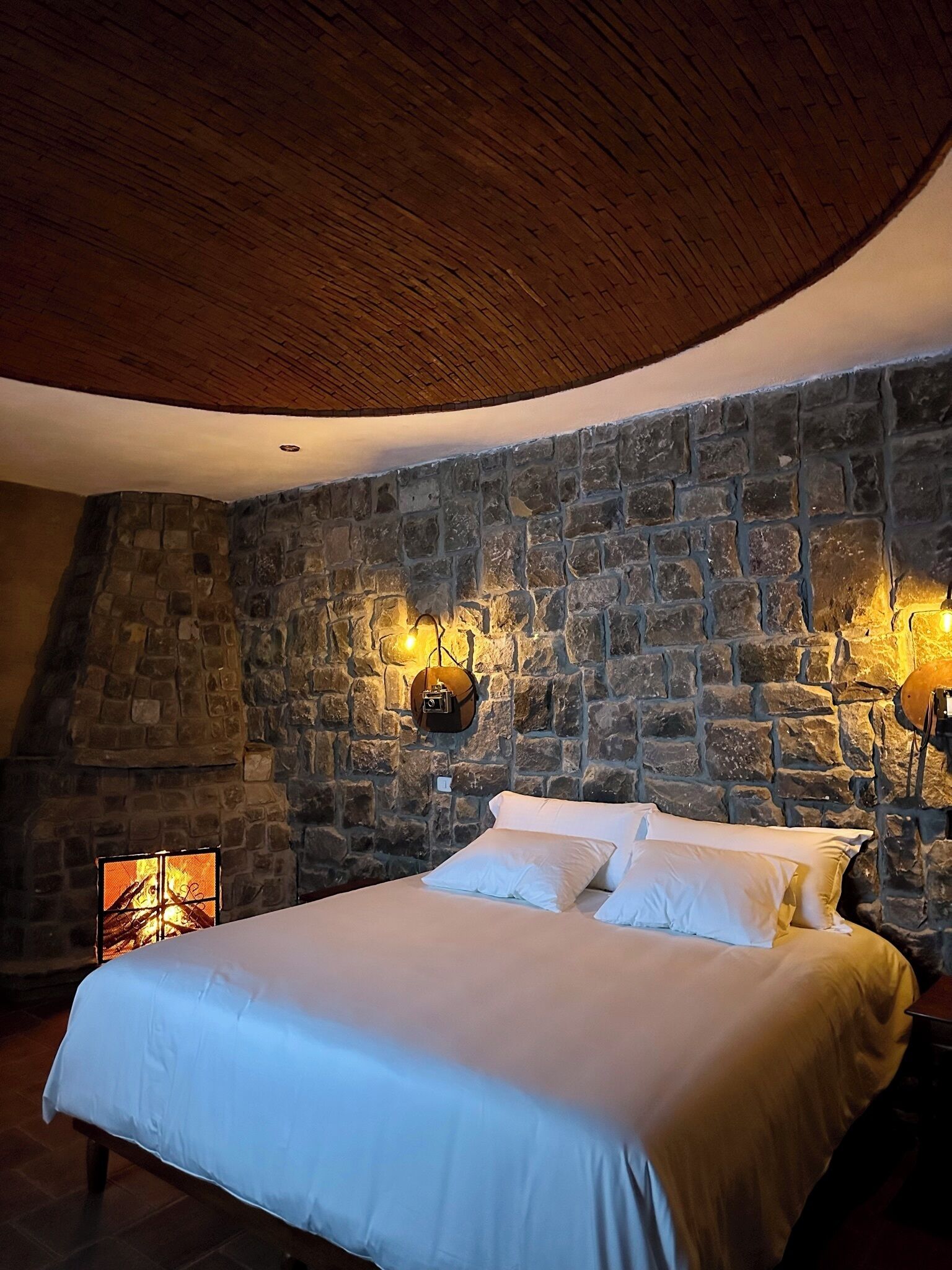 Un dormitorio con pared de piedra, techo de madera y cama con ropa de cama blanca.
