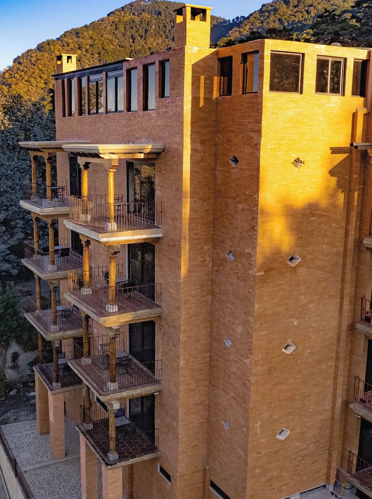 A multi-story building with balconies and large windows, surrounded by a mountainous landscape.