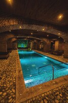 Una piscina interior con suelo de piedra y paredes de ladrillo, con una pared verde que presenta un diseño de mosaico al fondo.