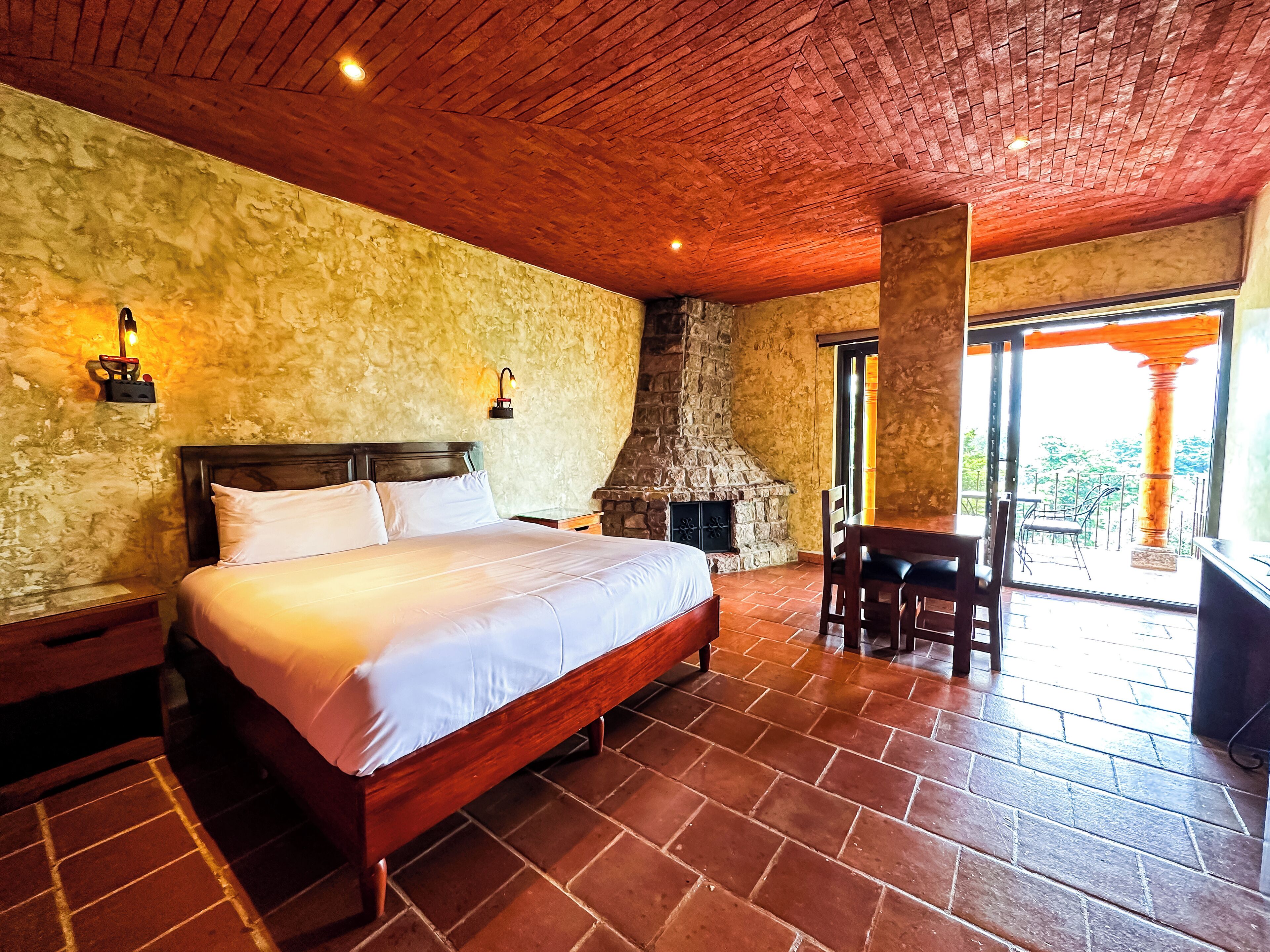A bedroom with a stone fireplace, a wooden bed, and a view of the outdoors through a glass door.