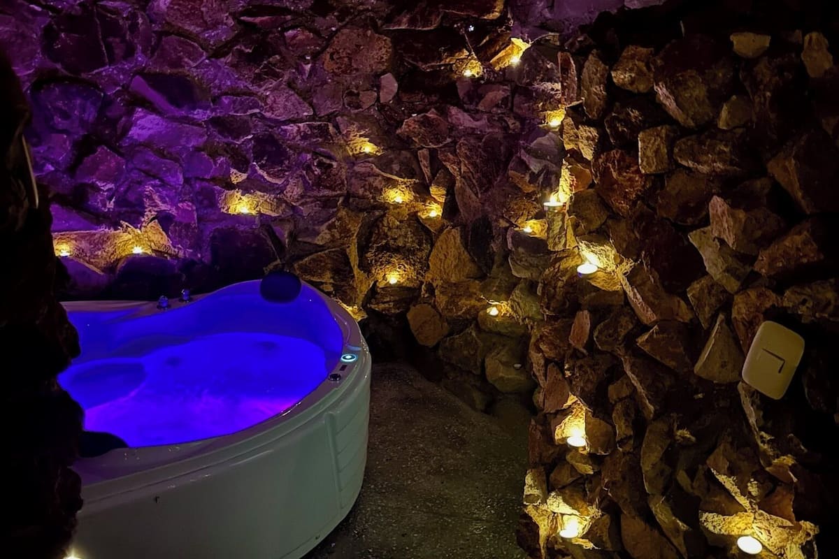 Un'area benessere con vasca idromassaggio, circondata da pareti in pietra e luci soffuse.