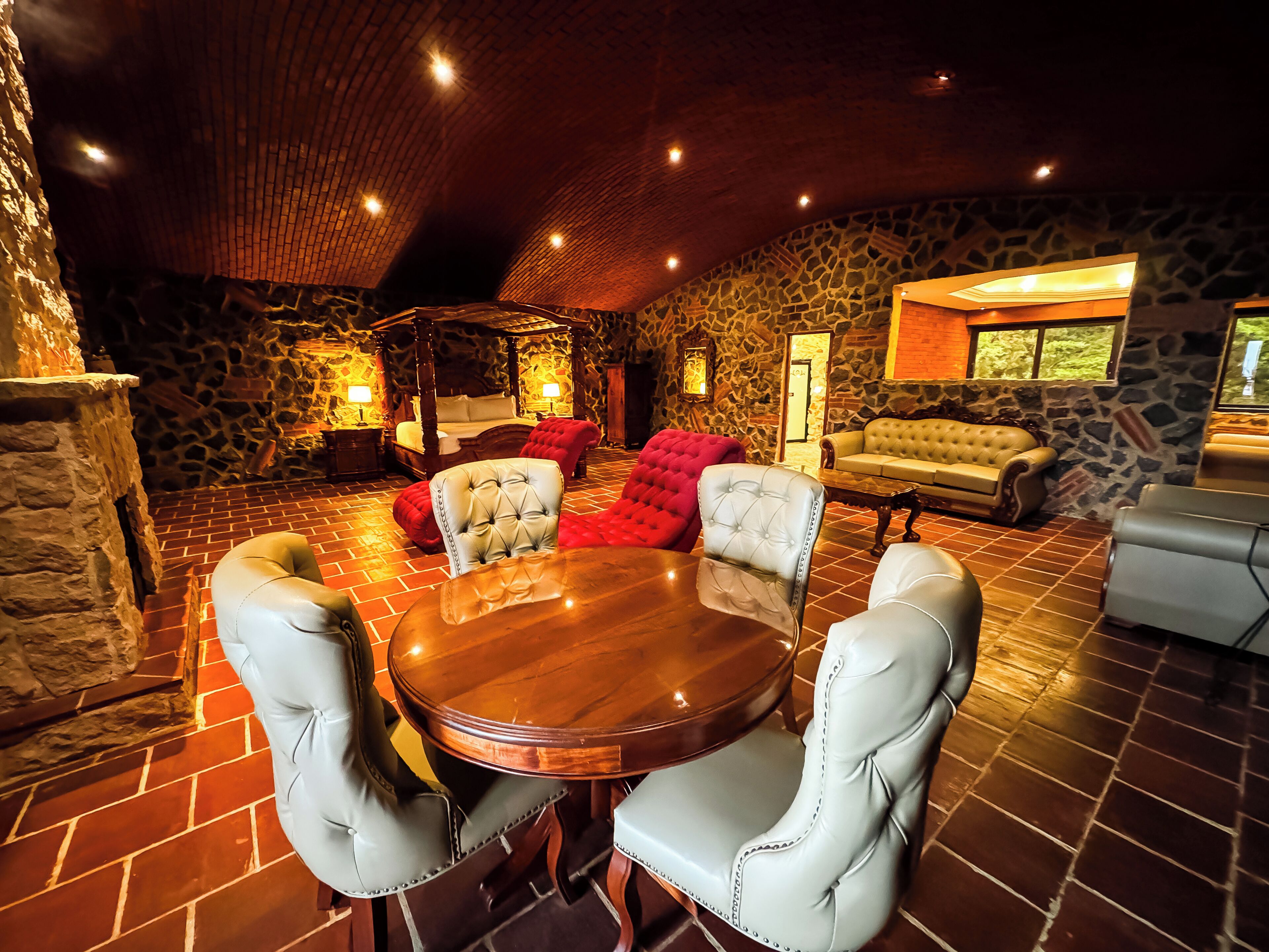 Una habitación amplia con pared de piedra, techo de madera y una gran mesa redonda con sillas.