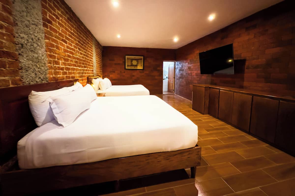 Una camera d'albergo con due letti, un muro in mattoni, una televisione a schermo piatto e un armadio in legno.