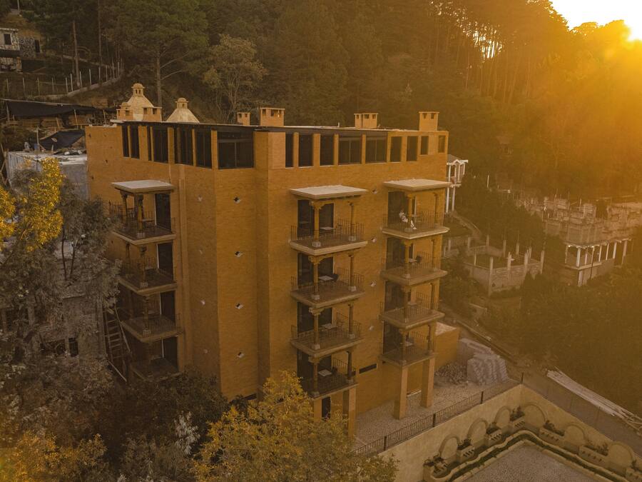 Un immeuble à plusieurs étages doté de balcons, situé près d’une étendue d’eau, avec un coucher de soleil en arrière-plan.