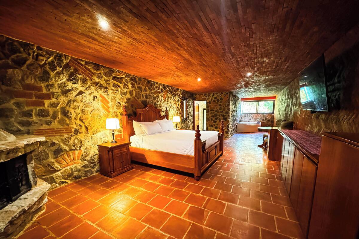 Una camera da letto con parete in pietra, soffitto in legno, un letto grande, un comodino, una TV e un camino in pietra.