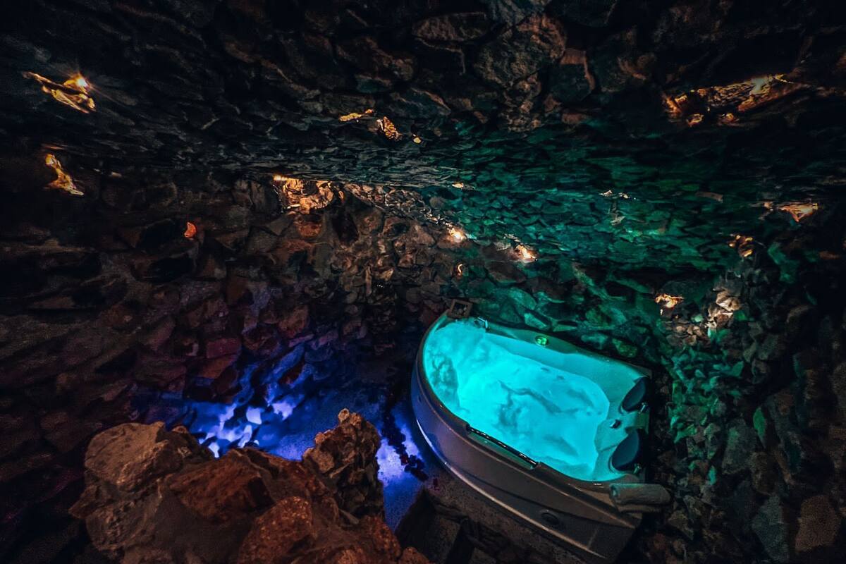 Un interno a grotta con una vasca idromassaggio circondata da rocce, illuminato da luci blu e verdi.