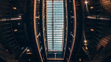 Un interior con un tragaluz central grande, una escalera circular y una zona de estar con plantas en macetas.
