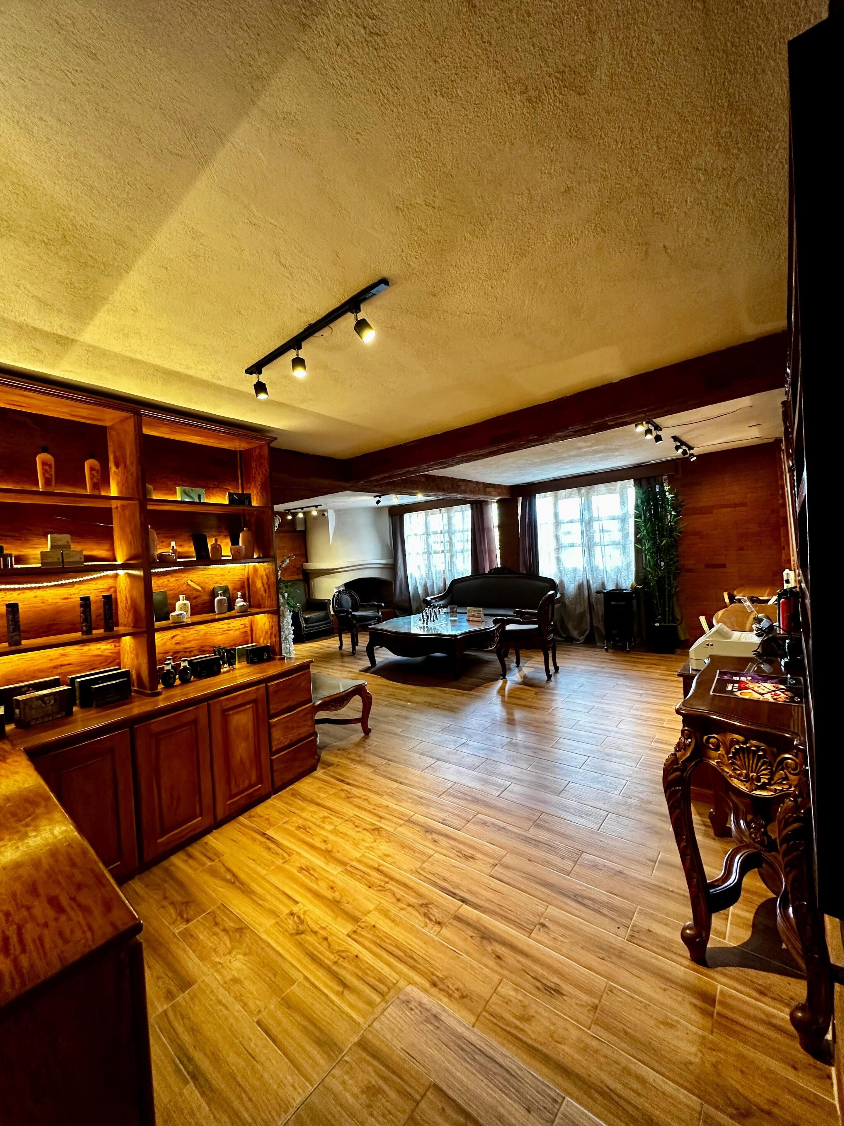 Un salón amplio con suelo de madera, una mesa de centro, un sofá y una estantería llena de objetos diversos.