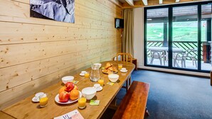 Un tavolo da pranzo in legno con prodotti per la colazione, una panca e vista su un paesaggio verde attraverso ampie finestre.