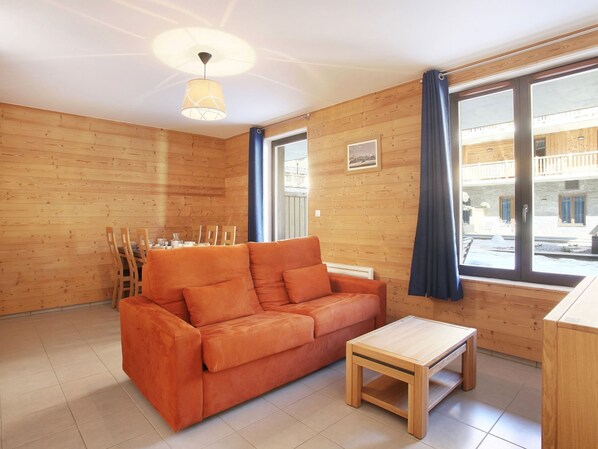 A cozy room with a wooden wall, a sofa, a small table, and a window with curtains.