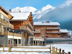A wooden chalet with multiple balconies, set against a snowy mountain backdrop.