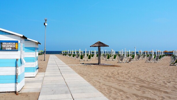 Une plage bordée de cabanes de plage, avec un sentier et des chaises de plage.