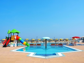 A swimming pool area with a water slide, play structures, and multiple umbrellas. - Rosapineta Sud by Interhome (Rosolina Mare)
