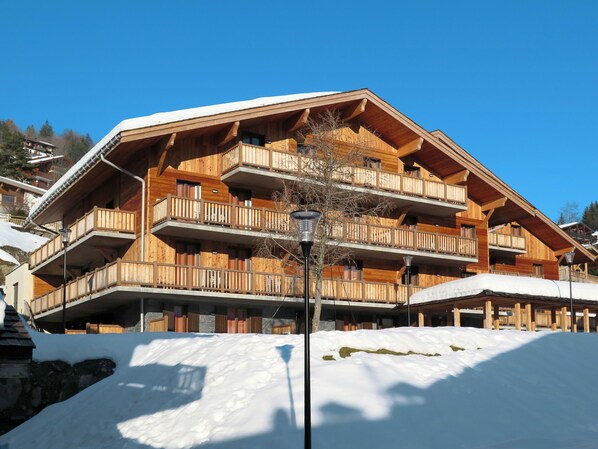 Un immeuble en bois à plusieurs étages, doté de balcons, et entouré de neige.