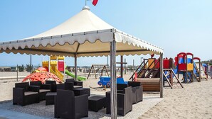 A beachside pavilion with a flag, children's play equipment, and seating areas.